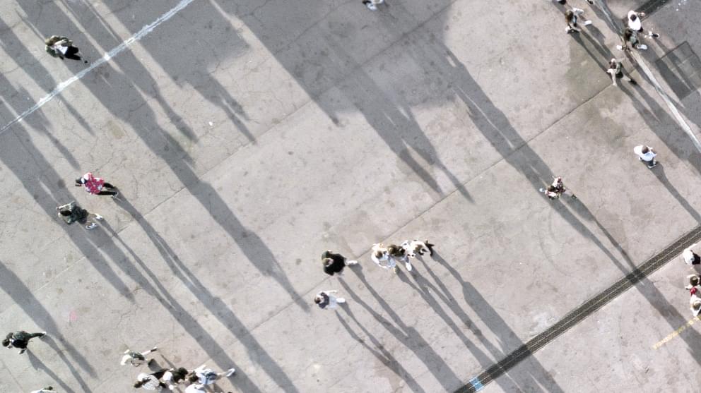 Aerial view of people walking across a concrete floor casting shadows