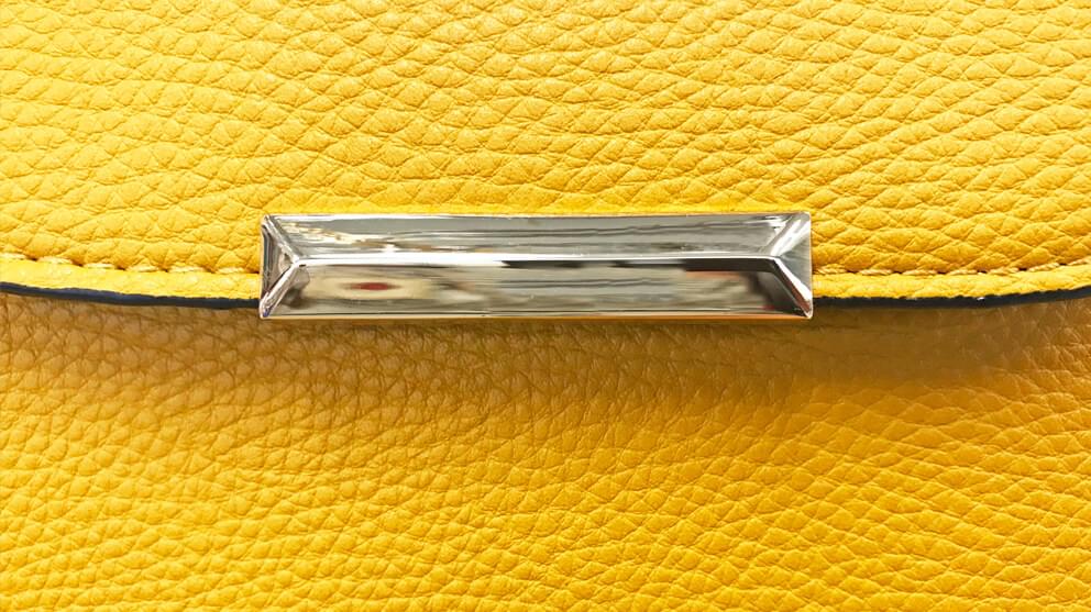 Details of a vibrant yellow ladies handbag with silver colored metal decor on flap